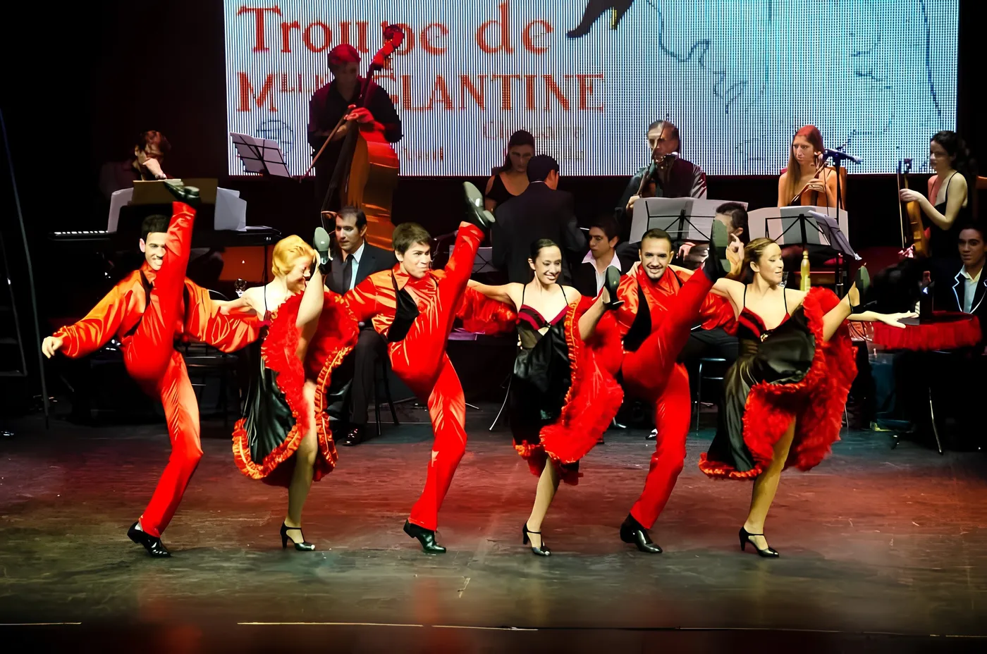 Bailarines de cancán con vestuario rojo y orquesta en vivo