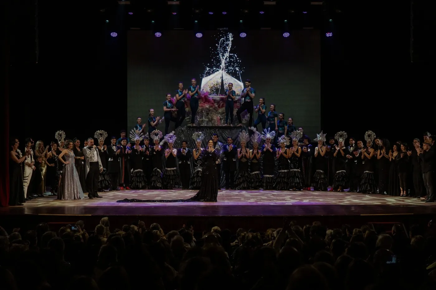 Elenco completo saludando en el escenario de un teatro