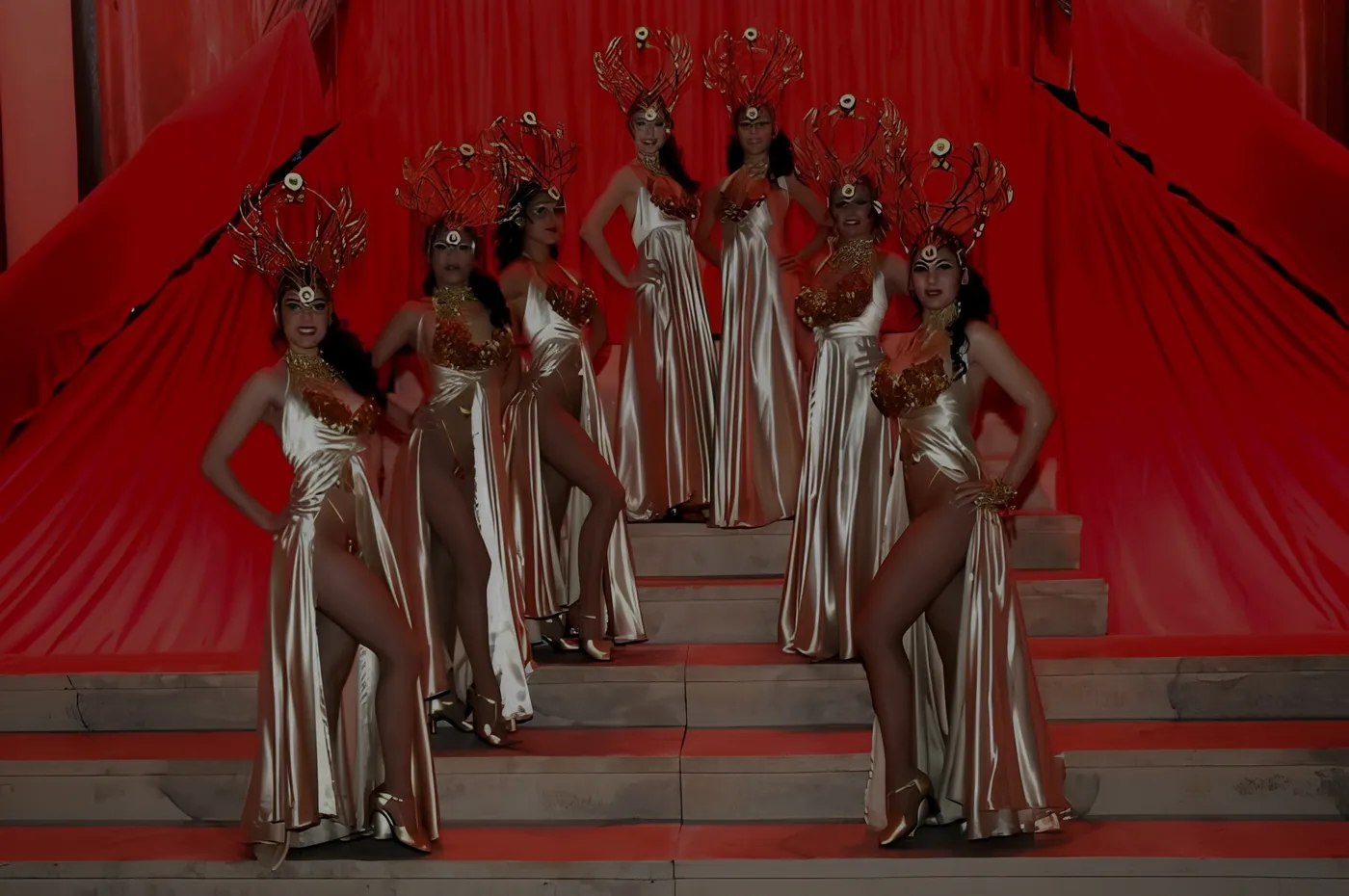 Bailarinas con trajes dorados y tocados de plumas sobre escenario rojo